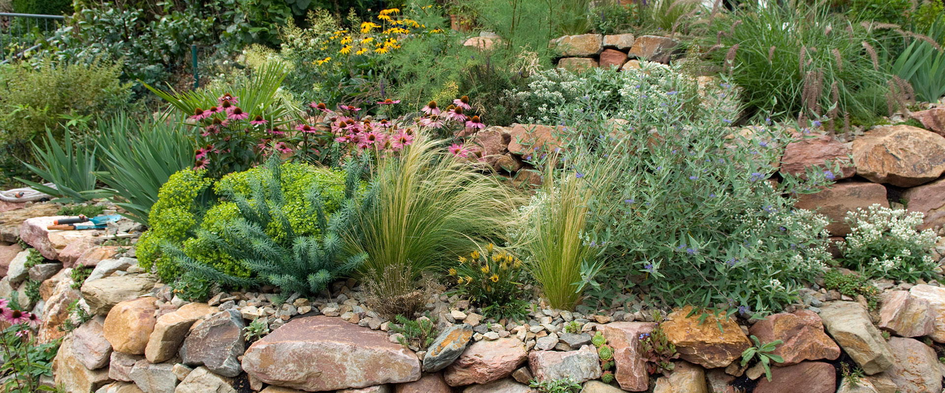 Sustainable tiered landscape with drought resistant flowers, plants, and grasses, with stone ground cover.
