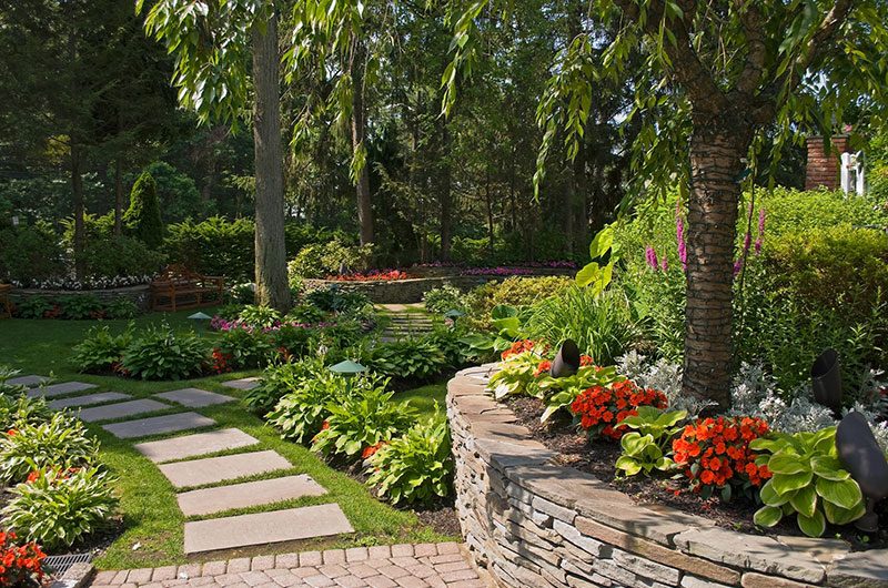 Park meticulously landscaped, with plants and flowers, trees, and stone walkways and borders.